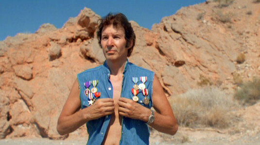 Neil Breen in Double Down standing proudly in a jean vest medaled with military awards one of which I think means he died in battle