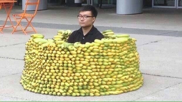 A guy sitting so peacefully, so tranquilly in the center of a fortress made entirely of stacked bananas