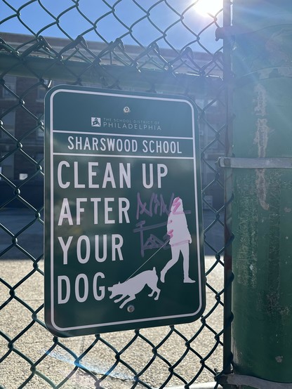 very official looking CLEAN UP AFTER YOUR DOG sign screwed to a fence but it's got a woman just looking away while her absolutely rabid dog loses its shit