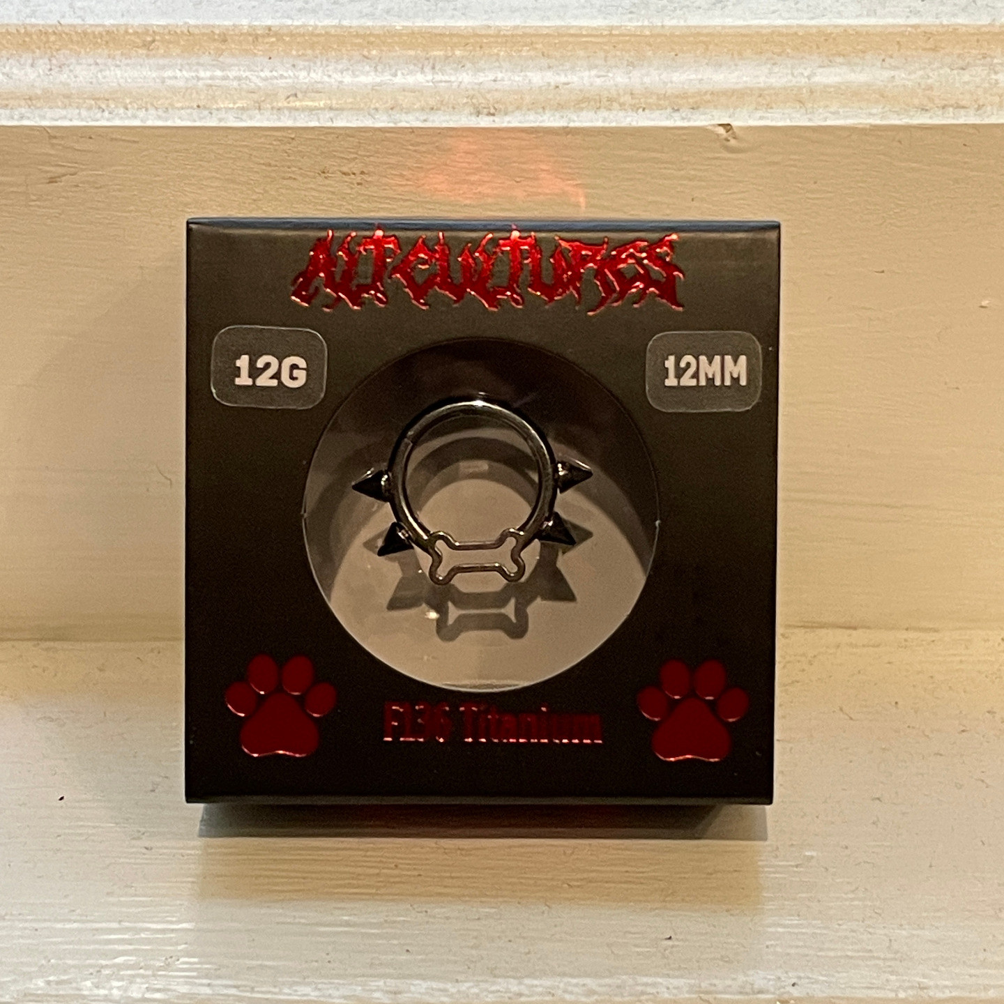 a terrible quality picture of a little black box with red paw prints containing a silver septum inside with mini spikes around the edge and a bone at the bottom